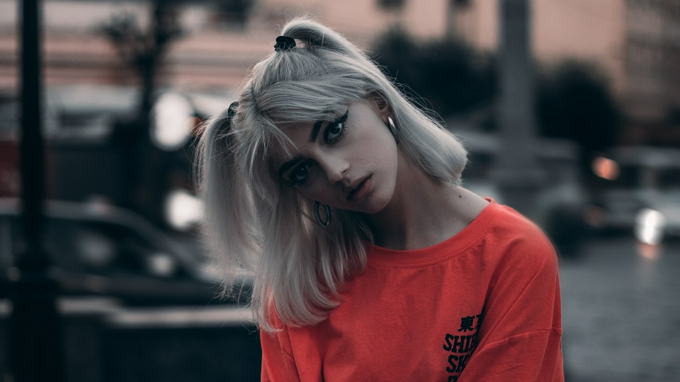 Девушка в оранжевой рубашке заплетает волосы в косу 4k